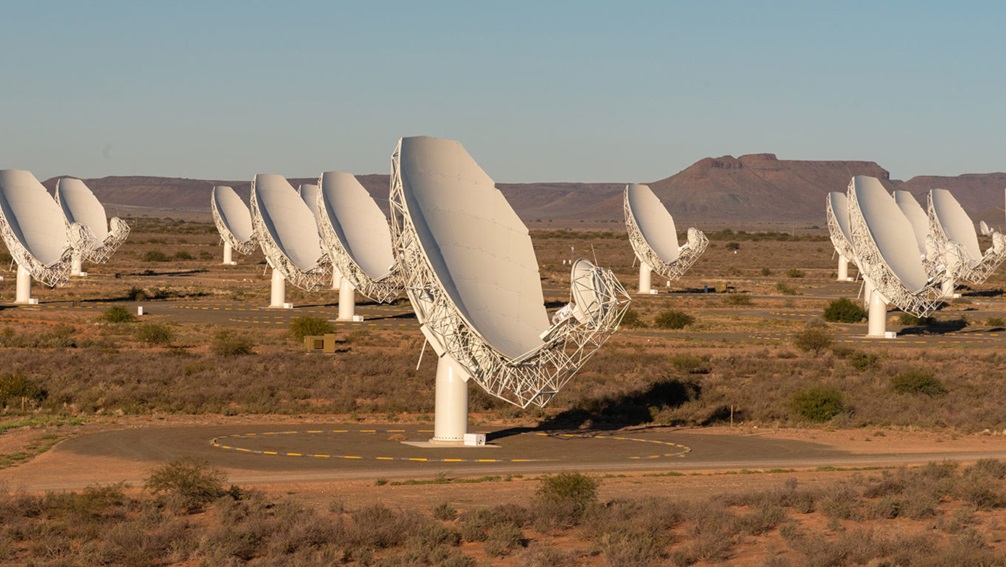 Looking out across a flat plane that features several large radio dish antenna all pointing towards the same direction of the sky.